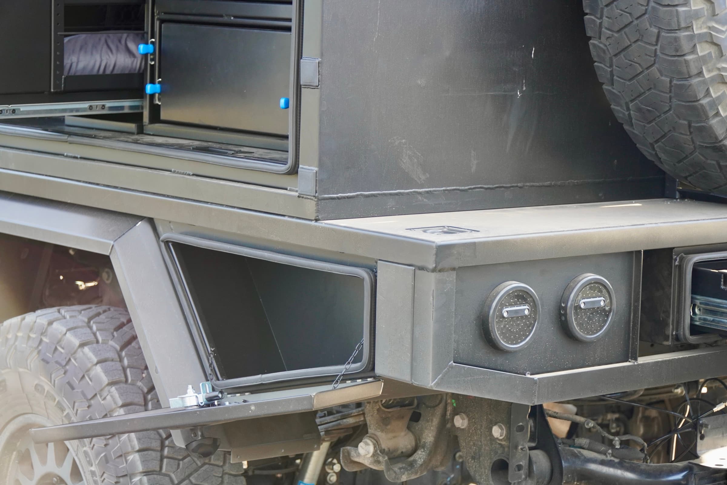 Closeup of the Ram 3500 under-tray toolbox dropped open on its chain stay, with canopy drawer slides and recessed deck tie-down points visible above